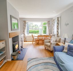 A living room with a fireplace a blue sofa a beige armchair a wooden dining table and windows with floral curtains at Manor Cottage in Embleton
