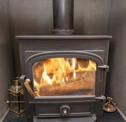 A wood burning stove with fire inside and brass candle holders beside it at Manor Cottage in Embleton