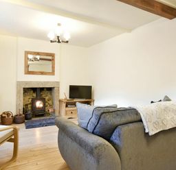 A living room with a gray sofa a wood-burning stove a wooden chair and TV at West End Cottage in Embleton