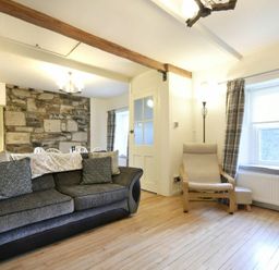 A living room with a gray sofa pillows a wooden armchair near a window and a stone wall at West End Cottage in Embleton