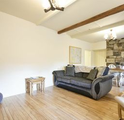 A living room with a grey sofa a wooden side table a blue knitted pouf and a dining table with chairs near a stone wall at West End Cottage in Embleton