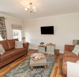 A living room with two brown sofas a wall-mounted TV a patterned rug and a checkered ottoman at The Bolthole (Seahouses) in Seahouses
