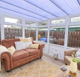 A sunroom with a brown sofa and armchair a wooden coffee table and windows overlooking a fenced yard at The Bolthole Seahouses