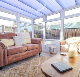 A sunroom with a brown sofa and wicker chair a wooden coffee table and large windows at The Bolthole (Seahouses) in Seahouses