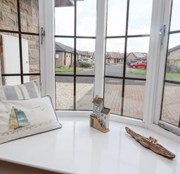 A window with a striped cushion a sailboat pillow and small wooden house decorations at The Bolthole in Seahouses
