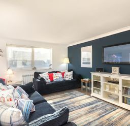 A living room with sofas and a television on a stand at Stones Throw in Beadnell