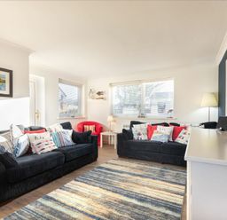 A living room with two black sofas and a red armchair with cushions a striped rug and a television at Stones Throw in Beadnell