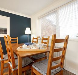 A dining room with wooden table and chairs next to a window with blinds at Stones Throw in Beadnell