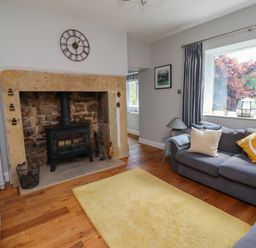 A living room with a stone fireplace and wood stove a sofa with cushions and a yellow rug at Alnside Cottage Alnmouth