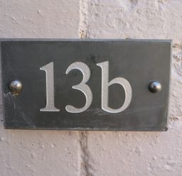 A black house number plaque with 13b attached to a textured light-colored wall at Riverside Lodge in Alnmouth