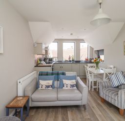 A kitchen and living area with a sofa, armchair, dining table, and flower vase at Riverside Lodge in Alnmouth