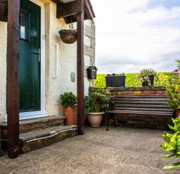 An outdoor seating area with a wooden bench potted plants and a green door at Swallows Cottage nr Warkworth in Acklington