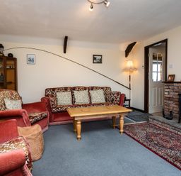 A living room with red velvet sofas a wooden coffee table a brick fireplace and a fishing rod on the wall at Swallows Cottage nr Warkworth in Acklington