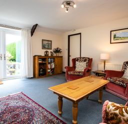 A living room with red patterned armchairs a wooden coffee table a wooden cabinet and French doors at Swallows Cottage nr Warkworth in Acklington