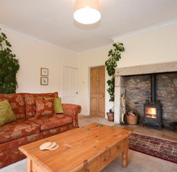 A living room with a floral sofa a wooden coffee table plants and a stone fireplace with a wood stove at Dunrovin in Beadnell
