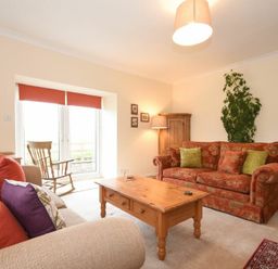 A living room with two sofas a wooden coffee table a rocking chair a tall plant and a wooden cabinet at Dunrovin in Beadnell