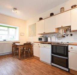 A kitchen with a wooden dining table and chairs a stove microwave dishwasher and cabinets at Dunrovin in Beadnell