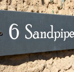 A black house number sign with white text reading 6 Sandpiper on a textured wall at Sandpiper (Alnmouth) in Alnmouth