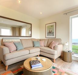 A living room with an L shaped sofa a round coffee table a large window with a sea view and a mirror on the wall at Portside in Seahouses
