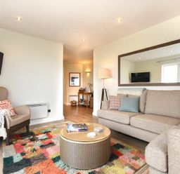 A living room with a beige sofa a round coffee table patterned rug an armchair and a large wall mirror at Portside in Seahouses
