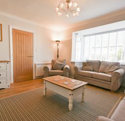 A living room with sofas a wooden coffee table a sideboard and a floor lamp at Anchor Lodge in Seahouses