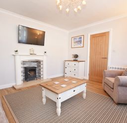 A living room with a wall-mounted TV fireplace coffee table and armchairs at Anchor Lodge in Seahouses
