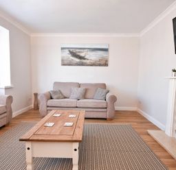 A living room with two sofas a wooden coffee table a carpet a fireplace and a wall painting at Anchor Lodge in Seahouses