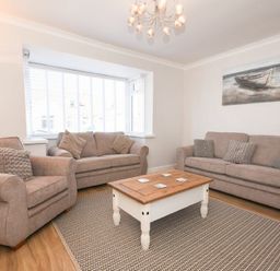 A living room with two sofas an armchair a coffee table and a beach painting at Anchor Lodge in Seahouses