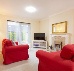 A living room with red sofas a white TV stand and a fireplace with a mirror above at Summerfold in Warkworth