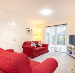 A living room with red sofas a white coffee table a television and vertical blinds at Summerfold in Warkworth