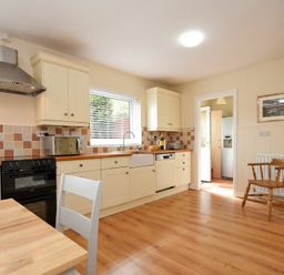 A kitchen with cream cabinets a black stove a wooden chair and a window at Summerfold in Warkworth