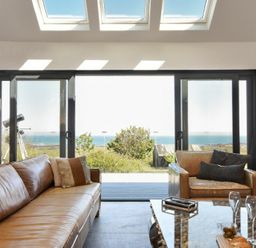A living room with leather sofas a telescope and sliding glass doors with a sea view at Waters Edge Beadnell Harbour Road in Beadnell
