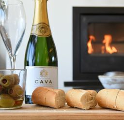 A bottle of cava with two champagne glasses a bowl of olives and three pieces of bread in front of a fireplace at Waters Edge Beadnell Harbour Road in Beadnell