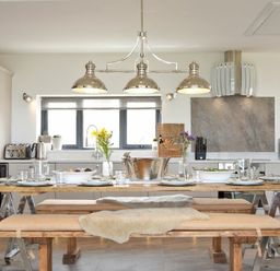 A kitchen with a wooden dining table set with plates glasses and flowers at Waters Edge Beadnell (Harbour Road) in Beadnell