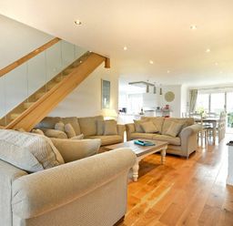 A living room with beige sofas a wooden coffee table a TV stand and a staircase with glass panels at Portland in Beadnell