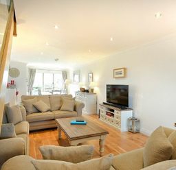 A living room with beige sofas a wooden coffee table a TV on a white stand and dining area visible at Portland in Beadnell