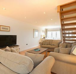 A living room with beige sofas a wooden coffee table a television and wooden stairs at Portland in Beadnell
