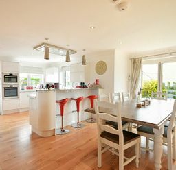 A kitchen and dining area with white cabinets red bar stools and a wooden dining table at Portland in Beadnell