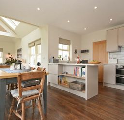 A kitchen and dining area with wooden chairs and table and kitchen island with books at South View nr Bamburgh in Seahouses