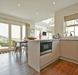 A kitchen with cabinets microwave toaster and a dining table with chairs near glass doors at South View nr Bamburgh in Seahouses