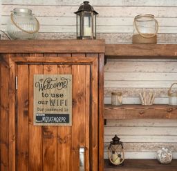 Wooden cabinet with a wifi password sign and wooden shelves with lanterns and glass jars in a room with striped walls at Rivershield in Warkworth