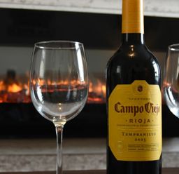 A bottle of Campo Viejo Rioja Tempranillo 2015 wine with two empty wine glasses in front of a fireplace at Rivershield in Warkworth