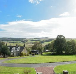 A rural landscape with a stone house trees grass and hills under a partly cloudy sky at The Lodge (Elsdon) in Elsdon