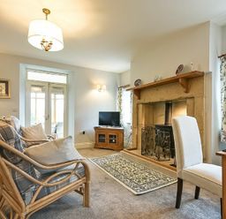 A living room with wicker chairs, a fireplace, a rug, a TV on a wooden stand, and a dining chair at The Lodge Elsdon