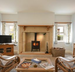A living room with a stone fireplace and wood stove two armchairs and a wooden table with magazines at The Lodge Elsdon