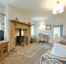 A living room with a TV on a wooden cabinet a fireplace a small desk with a chair and two armchairs at The Lodge (Elsdon) in Elsdon