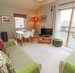 A living room with a sofa, dining table, and television at Cuddy's Holm in Seahouses