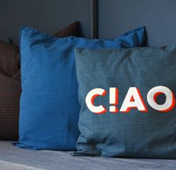 A set of four pillows on a sofa with one pillow displaying the word CIAO