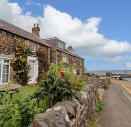 An outdoor area with stone walls and flowers at Coble Cottage in Craster