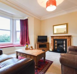 A living room with two brown sofas a wooden coffee table a fireplace and large bay windows at Sunnybrae in Alnmouth